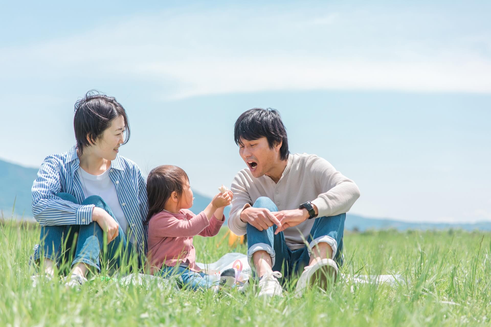 草原のピクニックで、女の子がお父さんにお菓子をあげている家族団らんの風景