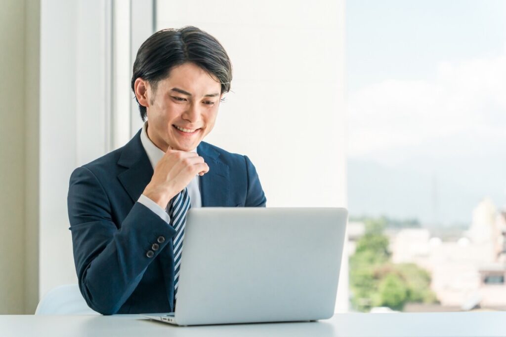 ノートパソコンを見ながらガッツポーズで喜ぶスーツ姿のビジネスマン