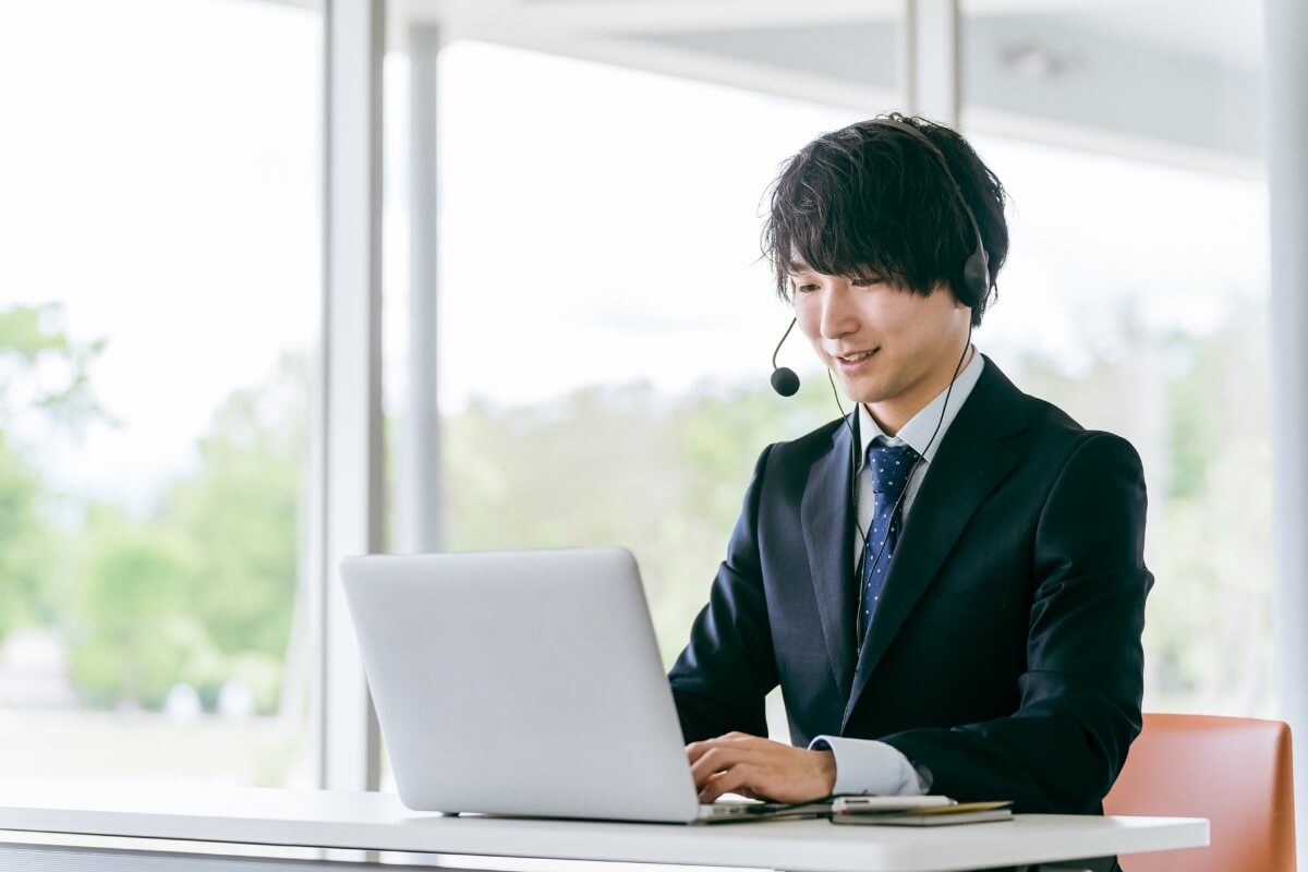 明るいオフィスでヘッドセットを着けてノートパソコンでオンライン会議をする笑顔のビジネスマン