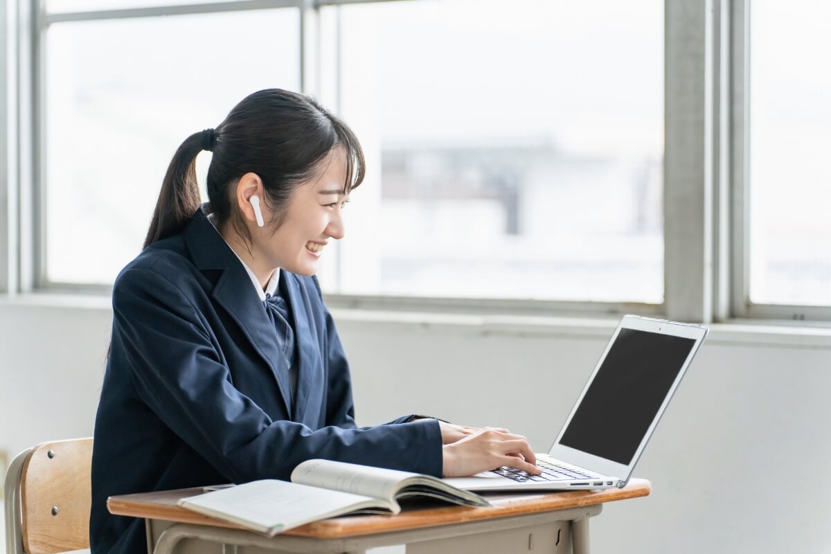 ワイヤレスイヤホンを着けてノートパソコンで学習する笑顔の女子学生