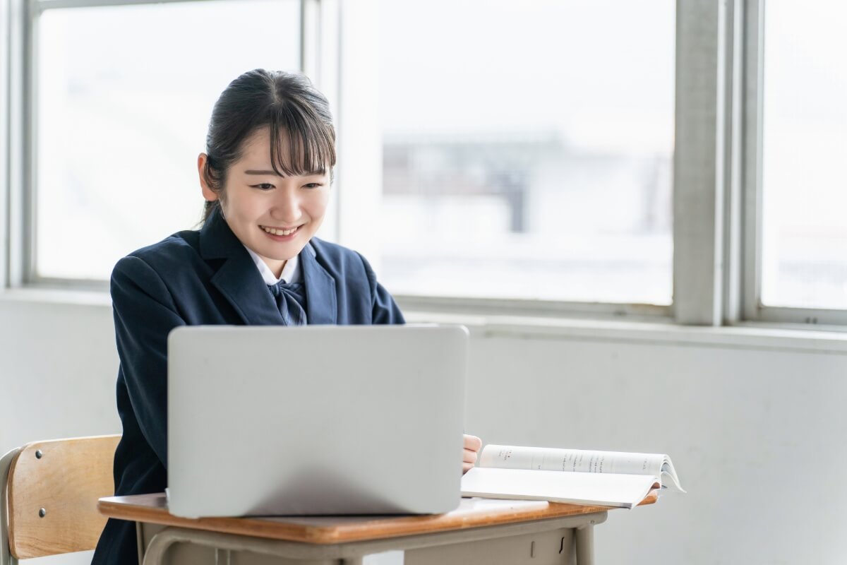 教室の机でノートパソコンを使って学習する笑顔の女子学生