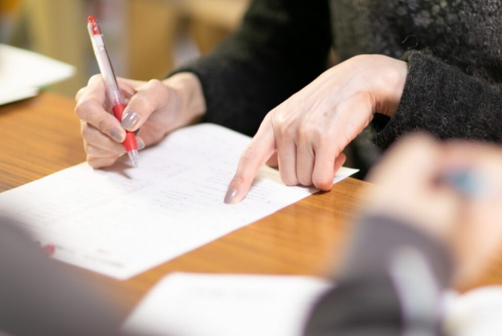 赤いペンでノートに書き込みをする学生の手元